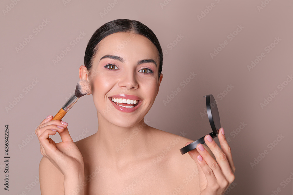 Beautiful young woman applying face powder with brush on dusty rose background Beautiful young woman applying face powder with brush on dusty rose background