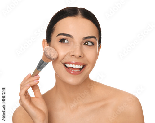 Beautiful young woman applying face powder with brush on white background