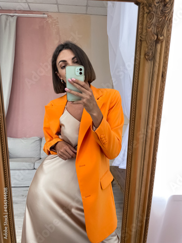 Bild auf Leinwand Fit tanned woman in romantic beige silk dress and orange blazer at home take pho