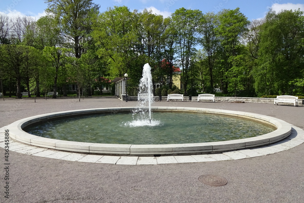 Fountain with clear water on a sunny day in Kardiorg park, Tallinn, Estonia. Benches and trees on the back. Fountain with clear water on a sunny day in Kardiorg park, Tallinn, Estonia. Benches and trees on the back.