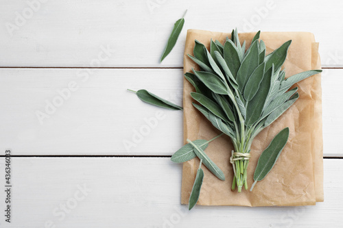 Bunch of fresh green sage with parchment on white wooden table, flat lay. Space for text photo