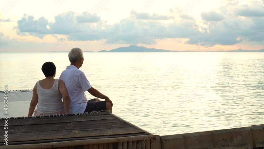 Asian senior couple sitting at sunrise sea early morning relaxed happy natural retirement Asian senior couple sitting at sunrise sea early morning relaxed happy natural retirement