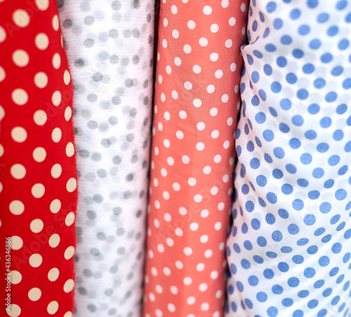 Close-up multicolored polka dotted fabrics linen cloth in rolls. Rows of minimalist red, blue and white colors. Sewing or tailoring concept. High quality vertical photo