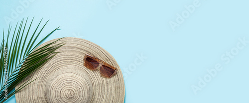 Women's hat with wide brim, sunglasses and a branch of a palm tree on a blue background. Summer concept, vacation at sea. Banner. Flat lay, top view