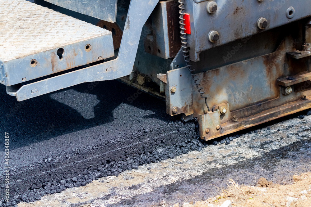 Asphalt paver on the road while laying asphalt, part of the car close up. Road repair. Laying a new road