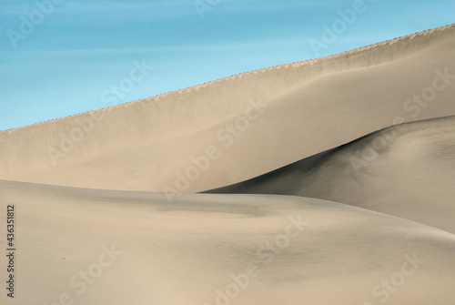 The smooth lines of sand dunes under the blue sky. Close-up.