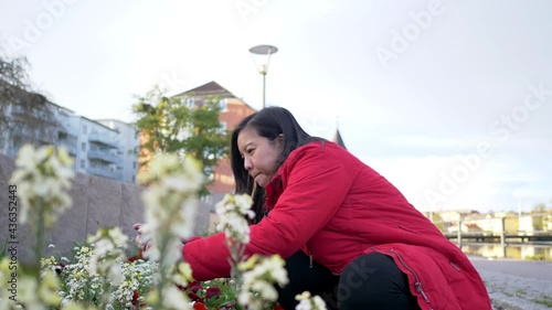 Asian womanwearing red coat sitting to take a picture of flower by the river, getting wonderful moment, feeling relax and seeing beautiful nature. River background. Going out for a walk photo