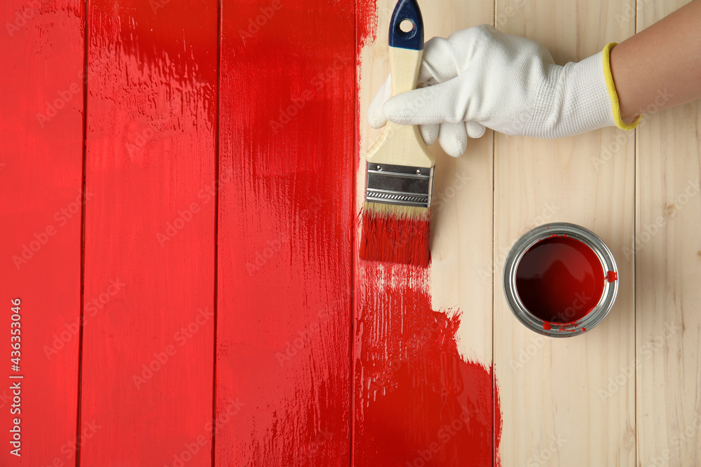 Worker in gloves painting wooden surface with red dye, top view. Space for text