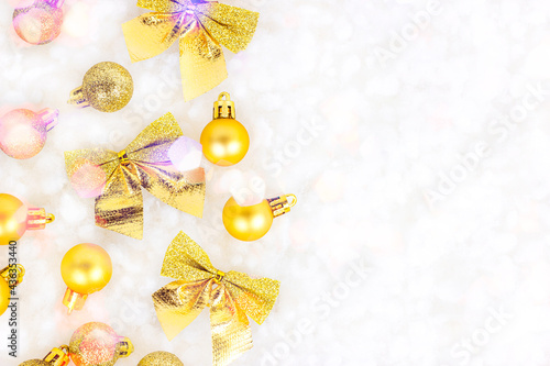 Bright golden Xmas decorations (ribbons, baubles, bows, ornament) flat lay on white artificial snow background with copy space. Christmas and New Year traditional holiday celebration concept.