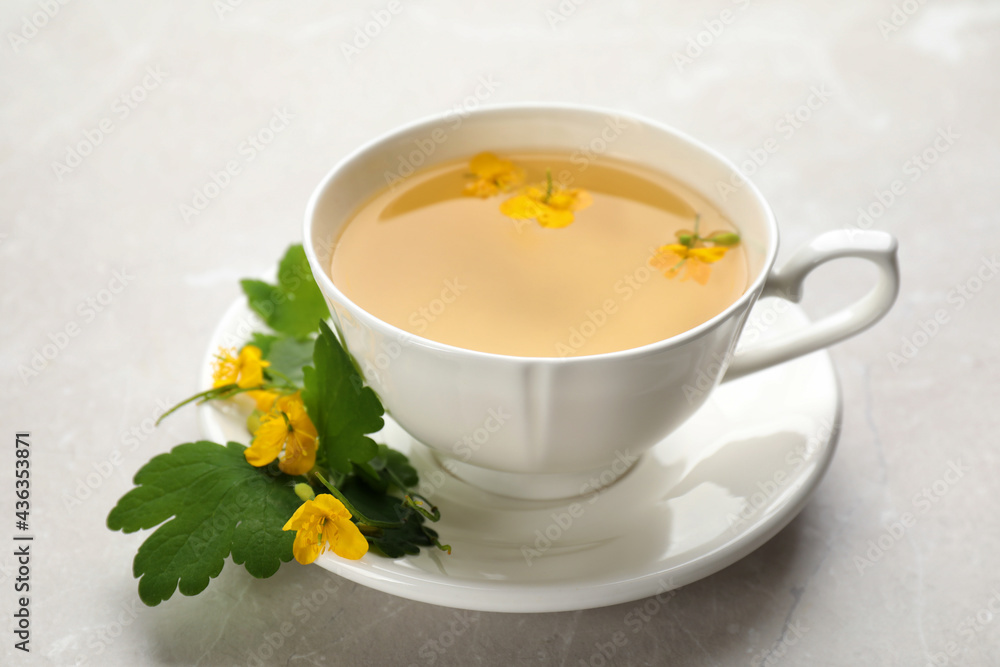 Cup of aromatic celandine tea and flowers on grey table, closeup Cup of aromatic celandine tea and flowers on grey table, closeup