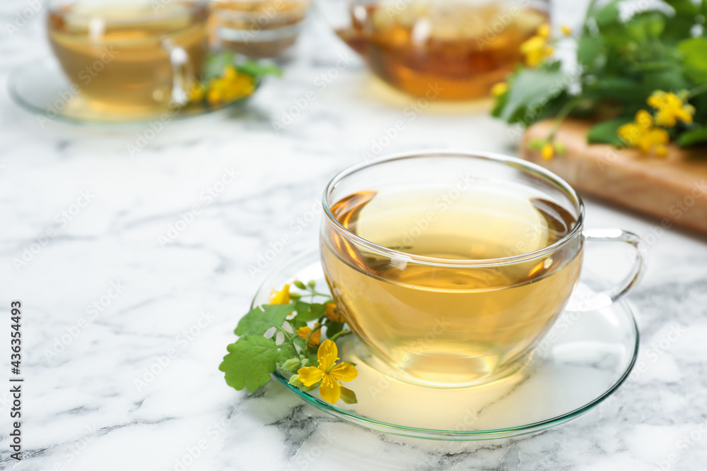 Glass cup of aromatic celandine tea and flowers on white marble table, space for text Glass cup of aromatic celandine tea and flowers on white marble table, space for text