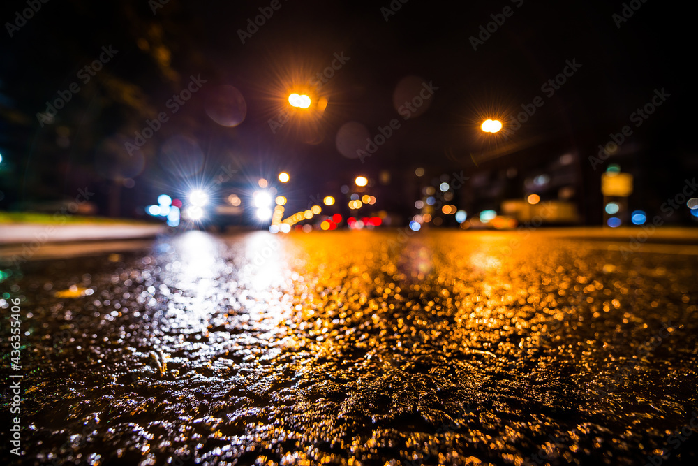 Night city after rain, approaching car headlights shine. View from a wide angle at the level of the asphalt