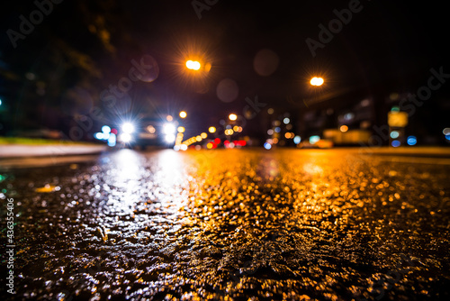 Night city after rain, approaching car headlights shine. View from a wide angle at the level of the asphalt