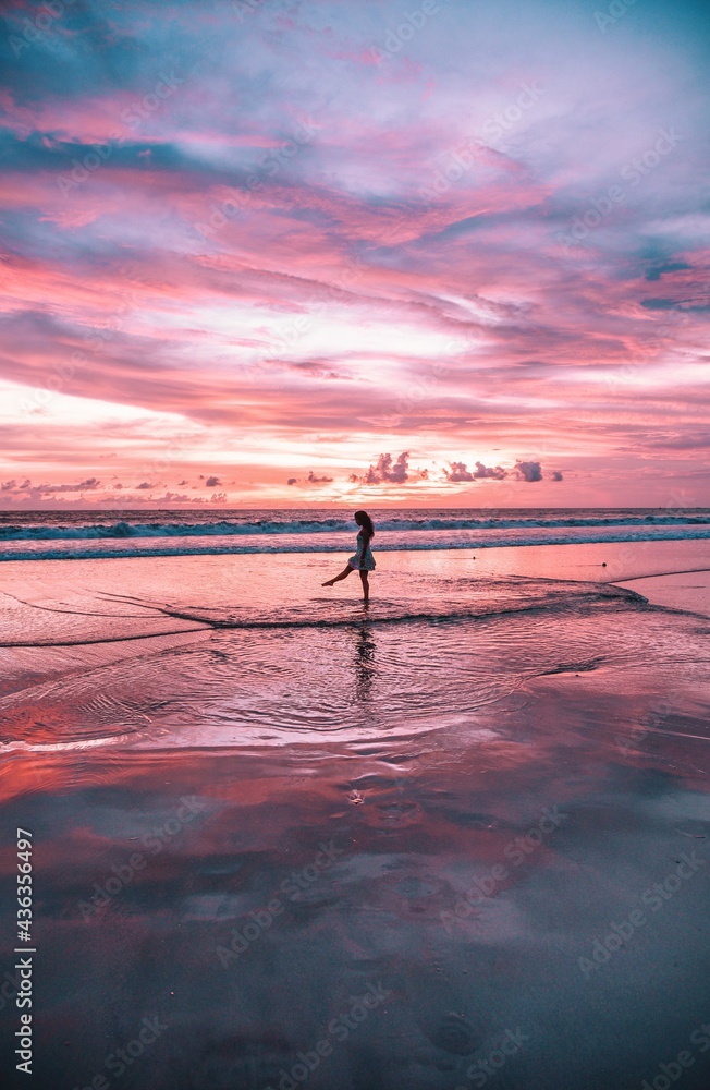 Women at sunset in Bali playing with the ocean water in front of purple and pink skies