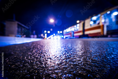 Night city after rain, the cars and tram driving on the road. View from a wide angle at the level of the asphalt