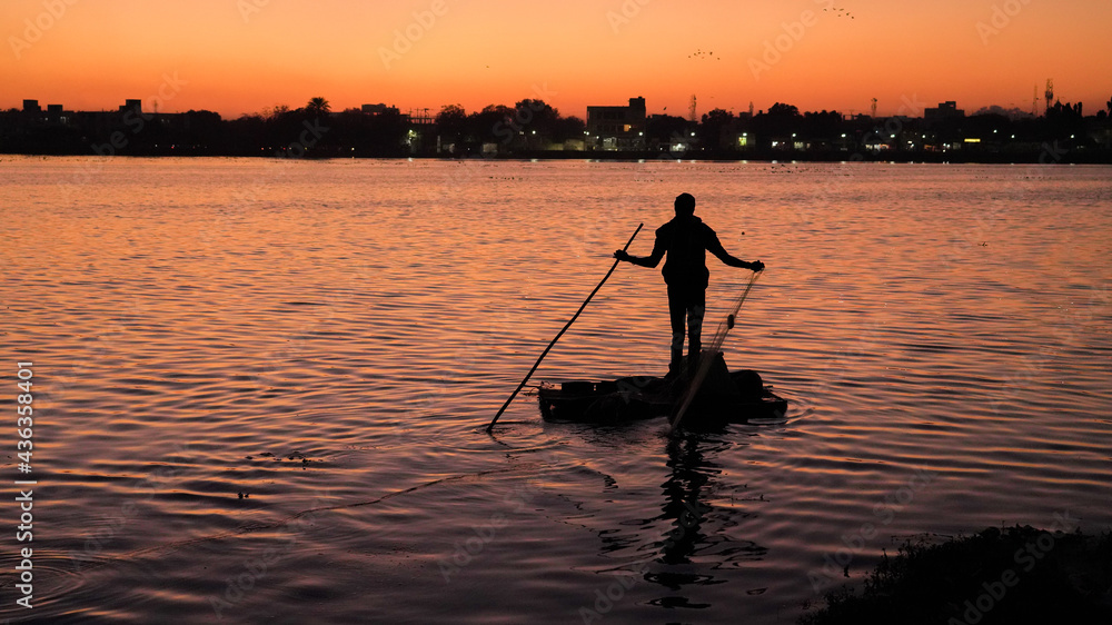 Fisherman on a small boat catching freshwater fish in nature river during sunset Fisherman on a small boat catching freshwater fish in nature river during sunset