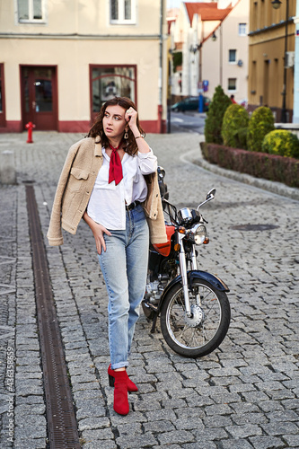 Obraz na płótnie Young beautiful woman in red knitted fabric block heel sock shoes, blue denim jeans pants and teddy jacket coat posing near a motorcycle on a street w salonie