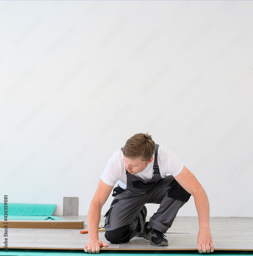 Worker in uniform lays the laminate in white room. White copy space for banner, promo Worker in uniform lays the laminate in white room. White copy space for banner, promo