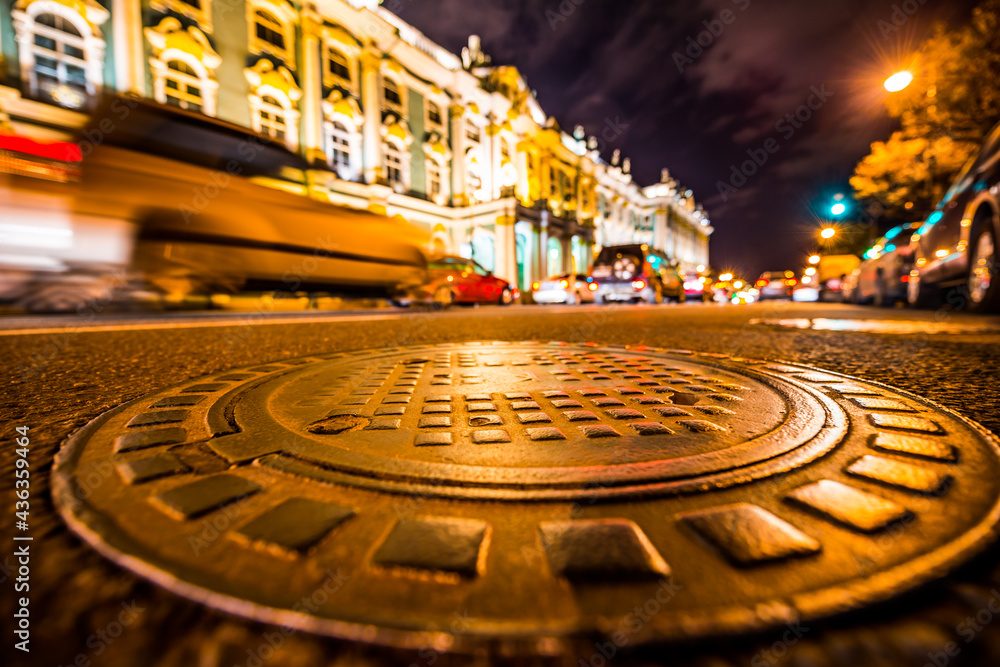 Lights of the city at night, cars are in traffic on the street. Wide angle view of the level of a manhole on the pavement