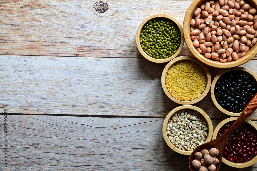 Dried peanuts, Hulled-split Mung Bean (Yellow beans), Mung Beans, Red beans, Black Beans, Millet grains are in the wooden bowl and Lotus seed in Wooden Spoon on the wooden table. Dried peanuts, Hulled-split Mung Bean (Yellow beans), Mung Beans, Red beans, Black Beans, Millet grains are in the wooden bowl and Lotus seed in Wooden Spoon on the wooden table.