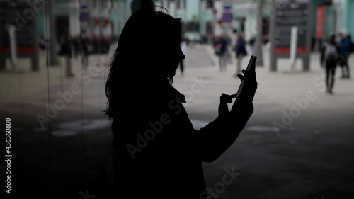 townswoman with smartphone in dark lane in downtown, walking and calling by cellphone photo