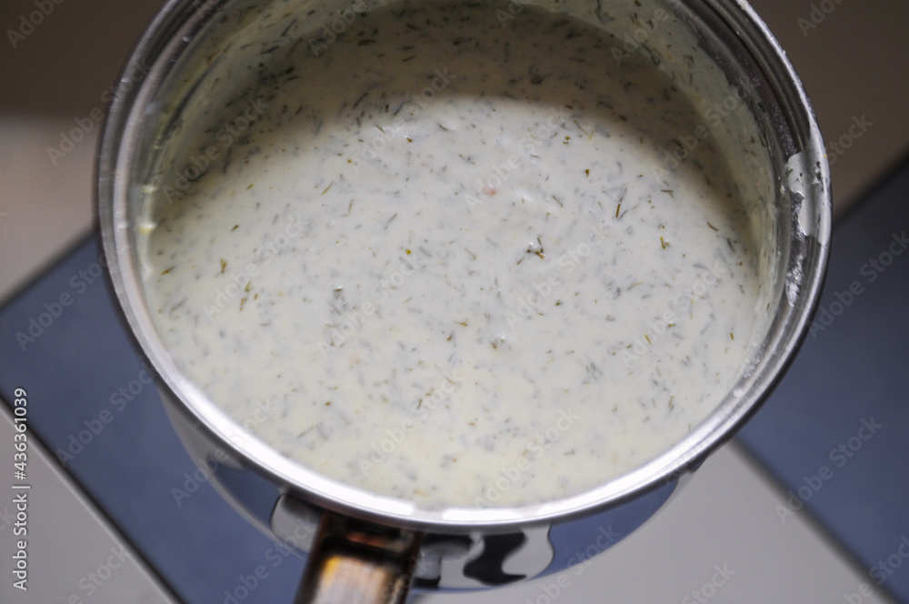 Béchamel sauce with dill in a saucepan on a background of white and blue tiles in the kitchen Béchamel sauce with dill in a saucepan on a background of white and blue tiles in the kitchen