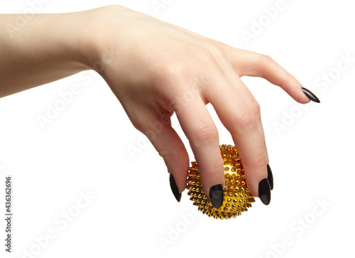 Female hand with black nails manicure and golden spiked massage ball in fingers.