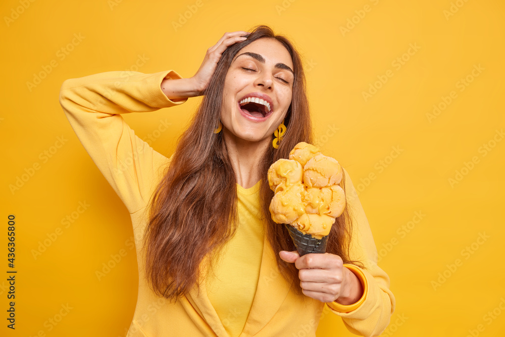 Φωτογραφία Beautiful carefree woman enjoys pleasant moment keeps eyes closed from pleasure mouth opened treats herself with tasty appetizing ice cream has fun during summer day isolated on yellow wall