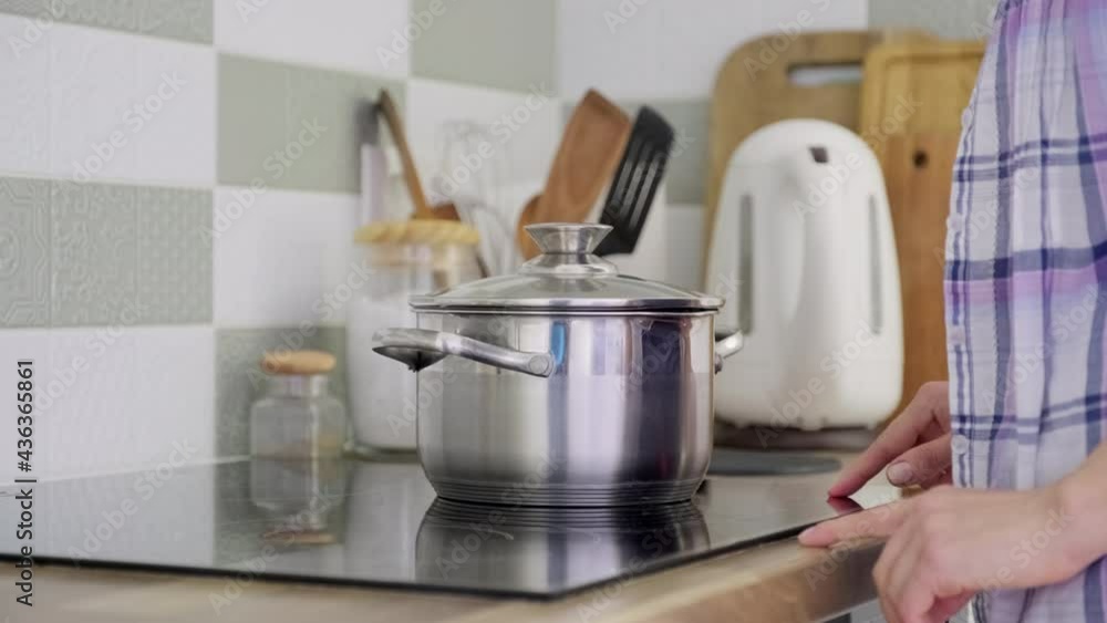 Woman's hands with saucepan on cooking glass ceramic surface, female turning on stove Woman's hands with saucepan on cooking glass ceramic surface, female turning on stove