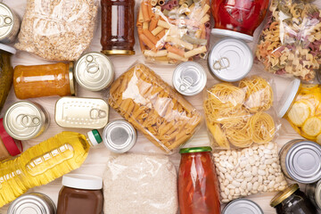 Food donations such as pasta, rice, oil, peanut butter, canned food, jam and other on white wooden table , top view