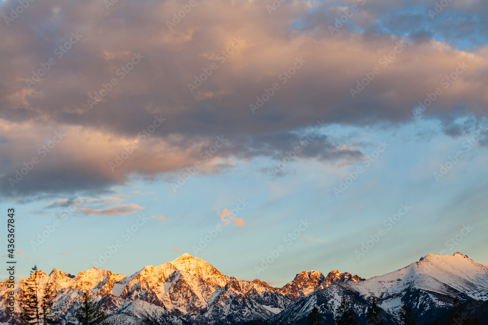 The setting sun illuminates the snow-capped peaks of the Tatra Mountains. Poland.