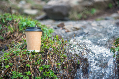 Close-up paper cup of coffee on mountain river background on top of the stone. For a coffee shop
