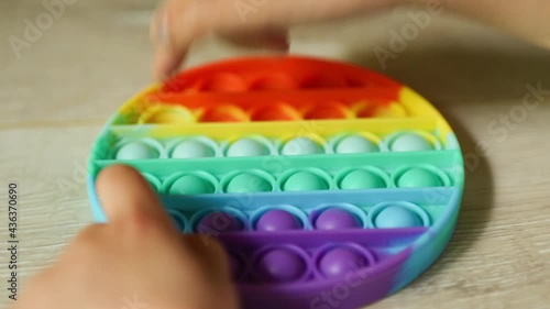 Child plays with touch anti-stress silicone pop it toy. Fingers press on rainbow soft bubbles and buttons. Trending game for development of fine motor skills and stress relief in children and adults photo