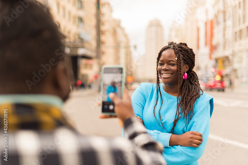 Black guy taking a photo with his mobile of his girlfriend.