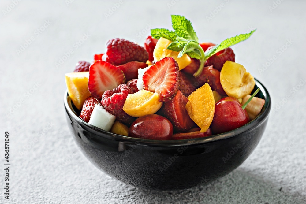 Fresh fruit salad in a black bowl on a gray background. Healthy natural organic food, low calories delicious dessert. Vegan concept Fresh fruit salad in a black bowl on a gray background. Healthy natural organic food, low calories delicious dessert. Vegan concept