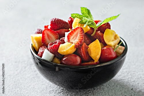  Fresh fruit salad in a black bowl on a gray background. Healthy natural organic food, low calories delicious dessert. Vegan concept