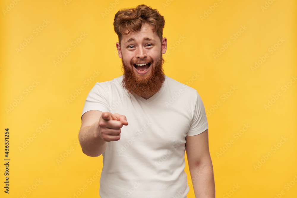 portrait of cheerful positive man with red beard wears blank t-shirt, laughing and point with a finger at the camera. isolated over yellow background portrait of cheerful positive man with red beard wears blank t-shirt, laughing and point with a finger at the camera. isolated over yellow background