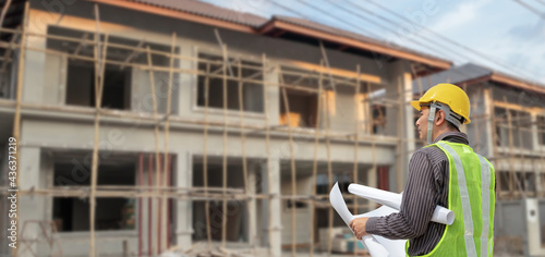 young professional engineer in protective helmet and blueprints paper at the house building construction site