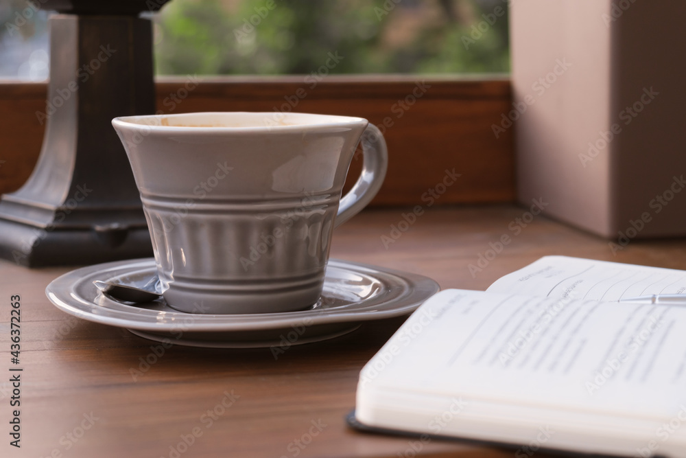 Still life with a gray ceramic cup of coffee on a saucer and an open diary with a pen. The concept of a business breakfast, business meeting in a cafe.