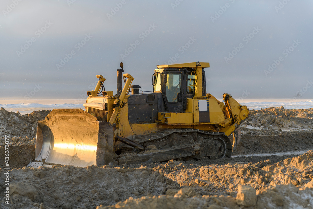 Yellow tractor in winter tundra. The road construction. Bulldozer.