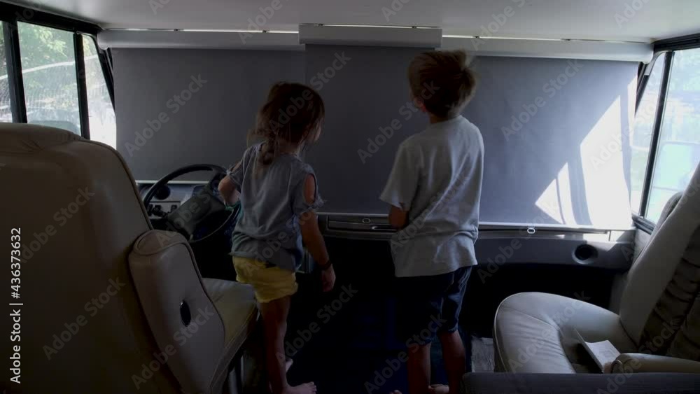 Two kids pulling down gray pull down blinds in an RV. Recreational car and two kids are pulling down the blinds.