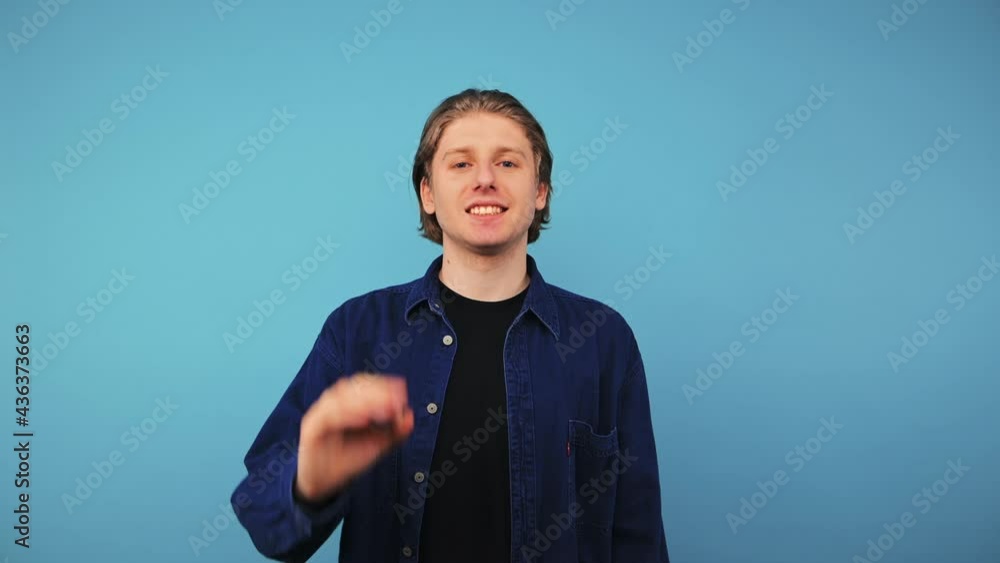 Positive young man in casual clothes stands on a blue background with a smile on his face winks and shows his fingers gesture OK, wears a shirt. Positive young man in casual clothes stands on a blue background with a smile on his face winks and shows his fingers gesture OK, wears a shirt.