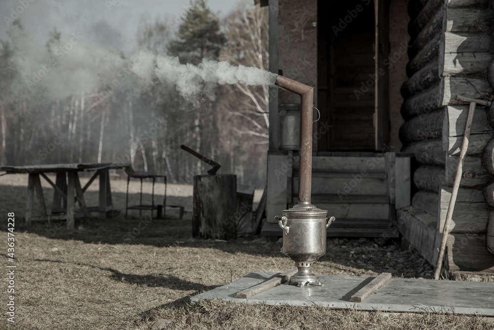 An old samovar heats water outdoors in the village. Smoke from the chimney. Sunny day. Rural nature. An old samovar heats water outdoors in the village. Smoke from the chimney. Sunny day. Rural nature.