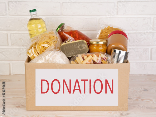 Food donations such as pasta, rice, oil, peanut butter, canned food, jam and other in a cardboard box on a white table