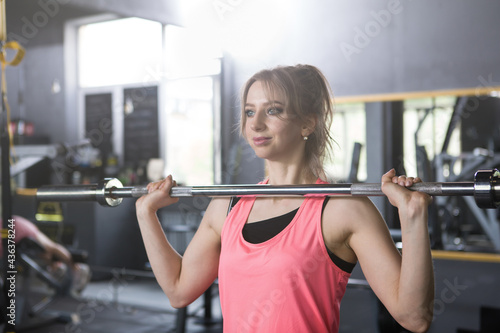 Cheerful young sportswoman doing barbell push press exercise at the gym