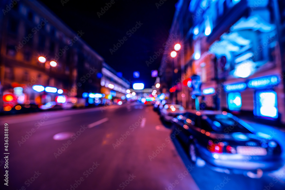Nights lights of the big city, night avenue in the light of lanterns and illuminated shop windows. Wide-angle view, defocused image