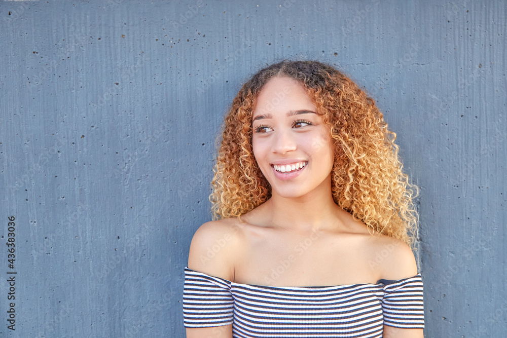 Fototapeta premium Smiling portrait of Latina teenager on gray background. Close-up of young girl with happy curly hair. 