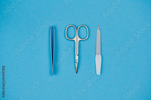 Nail scissors  tweezers and nail file are in the middle on blue background