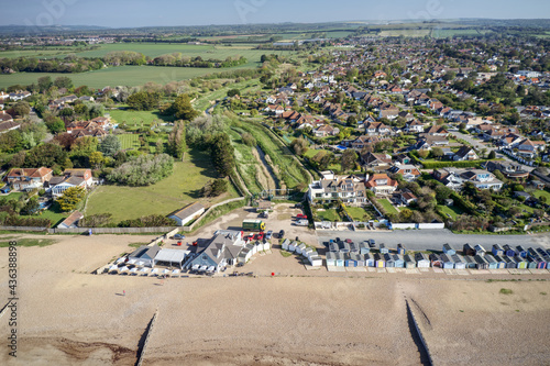 Ferring seafront on the English Channel with the Ferring Rife running next to the village of Ferring and towards the Beach Huts and coastline. Aerial view.