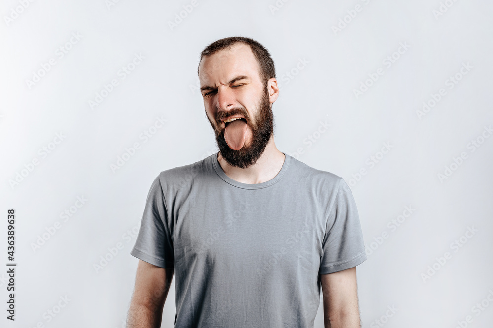 Handsome young brunette man frowning and closing eyes and sticking out tongue, angry on white background with space for advertising mock up Handsome young brunette man frowning and closing eyes and sticking out tongue, angry on white background with space for advertising mock up